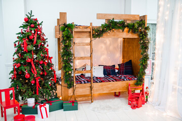 Bright festive children's bedroom with a two-story wooden bed with a ladder, decorated with a pine and fir garland. Christmas tree with red ornaments and boxes of presents under it. Christmas mood.