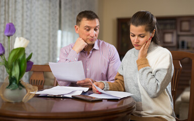Fototapeta na wymiar Loving couple looking worriedly at papers analyzing their finances at home..
