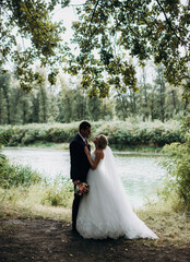 Wedding portrait of smiling newlyweds. Stylish groom in a blue suit and a cute blonde bride in a...
