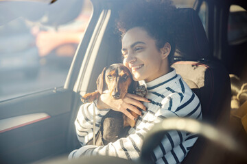 A young happy woman is hugging her dog in a car.