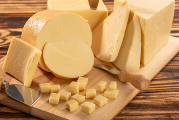 Cheeses, beautiful pieces of cheese and accessories placed on rustic wood, light background, selective focus.