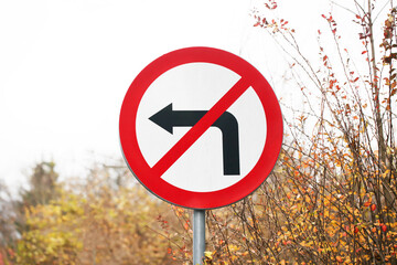 No turning left road sign. Autumn nature. Simple traffic sign background. Direction arrow.