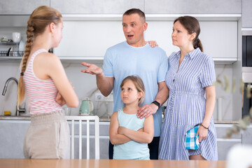 Disgruntled parents standing with preteen daughter in home kitchen, reprimanding eldest teenage girl. Emotional abuse concept