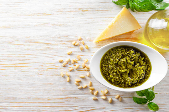 Homemade pesto sauce in small jar and ingredients for pasta on white wooden background with copy space. Traditional Italian cuisine, recipe, restaurant menu