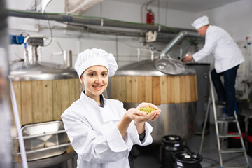 Smiling woman brewer holding bunch of hop pellets and looking at camera.