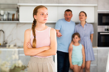 Daughter is standing next to table, turned back to parents during family quarrel. In kitchen, parents scold daughter for unreasonable behavior, spending money, returning home late