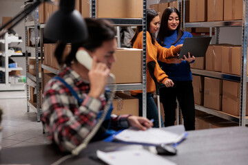 Warehouse employees using inventory management system software on laptop for checking product in stock. Postal service storehouse workers tracking parcel shipping online in storage room