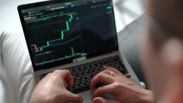 man businessman investor trader trades on bitcoin crypto exchange during a bull market, close-up hands typing on laptop keys, chart and candles of crypto market, investment