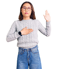 Young beautiful chinese girl wearing casual clothes swearing with hand on chest and open palm,...