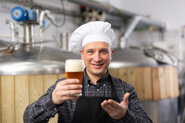 Portrait of brewer who is standing with glass of beer on his workplace in the brew-house