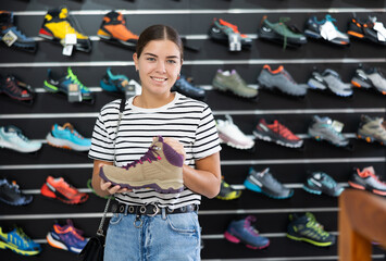 Young woman chooses specialized shoes in store, near showcase with tracking cross-shoes, buyers...