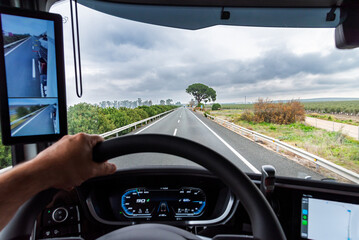 View from the driving position of a truck on a highway next to the field, a vehicle equipped with...