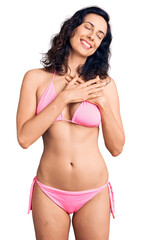 Obraz premium Young beautiful hispanic woman wearing bikini smiling with hands on chest with closed eyes and grateful gesture on face. health concept.
