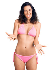 Naklejka premium Young beautiful hispanic woman wearing bikini smiling cheerful with open arms as friendly welcome, positive and confident greetings