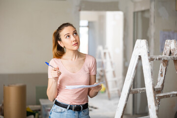 Portrait of young adult woman architect working with plan of house being renovated, developing concept of space planning