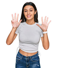 Young hispanic girl wearing casual white t shirt showing and pointing up with fingers number nine while smiling confident and happy.