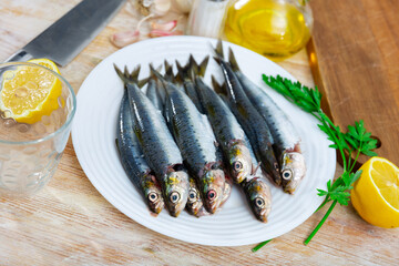 Fresh sardines lying on white plate with lemon, parsley and garlic