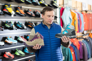 Attentive male athlete chooses sports winter shoes for hiking in a sports store