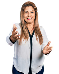 Middle age latin woman wearing business shirt looking at the camera smiling with open arms for hug. cheerful expression embracing happiness.