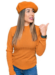 Young hispanic woman wearing french look with beret smiling with happy face looking and pointing to the side with thumb up.