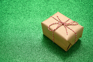 Caja de regalo de color marrón cerrada con lazo sobre fondo verde de purpurina