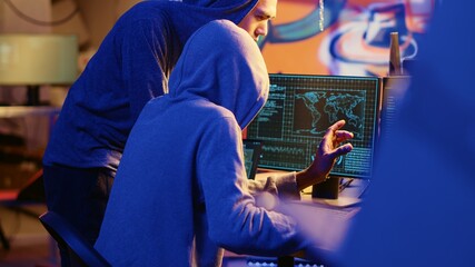 Hacking group founder initiating new member, showing him how to destroy firewalls and infect victim computer in hideout. Evil cybersecurity guru teaches script kiddie how to write malware code - obrazy, fototapety, plakaty