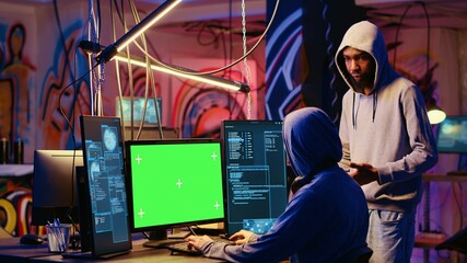 Hacker using green screen PC to do data breaches and financial theft in graffiti painted hideout. Rogue programmers using chroma key monitor for stealing users bank account credentials