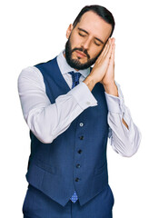 Young man with beard wearing business vest sleeping tired dreaming and posing with hands together while smiling with closed eyes.