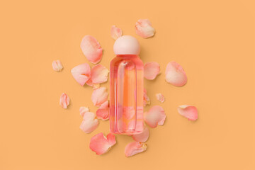 Bottle of cosmetic oil with rose extract and petals on orange background