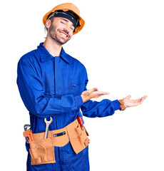 Young hispanic man wearing worker uniform inviting to enter smiling natural with open hand
