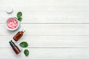 Podiums with bottles of essential oil and rose petals on white wooden background