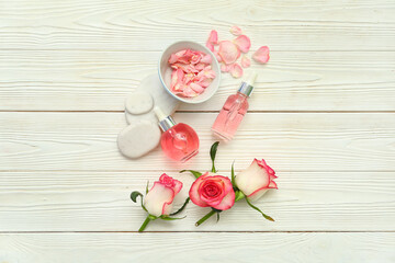 Stone podiums with bottles of essential oil, rose flowers and bowl on beige wooden background