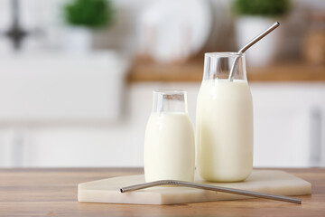 Glass bottles of fresh milk with straws on wooden table - obrazy, fototapety, plakaty