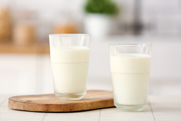 Wooden board with glasses of fresh milk on white tile table