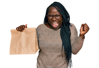 Young black woman with braids holding take away paper bag screaming proud, celebrating victory and...
