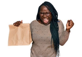 Young black woman with braids holding take away paper bag screaming proud, celebrating victory and success very excited with raised arms