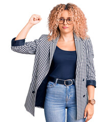 Young blonde woman with curly hair wearing business jacket and glasses strong person showing arm...