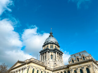 Fototapeta na wymiar Rear views of the Illinois State Capitol Building in Springfield, Illinois, USA. Cloudy blue skies overhead. Sunlight shines down upon the dome of the building.