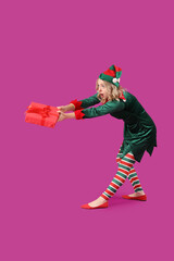 Emotional young woman dressed as elf with Christmas gift on purple background