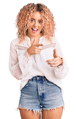 Young blonde woman with curly hair wearing elegant summer shirt pointing fingers to camera with happy and funny face. good energy and vibes.