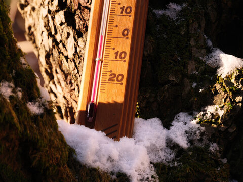 A meteorology thermometer shows 0 degree Celsius low cold temperature amidst December Christmas celebration and cool snowy winter weather season, placed on the white snow on the brown trunk of a tree.