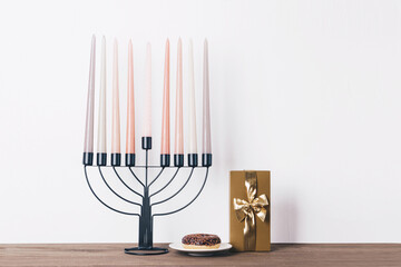 Black hannukia candlestick with nine multicolored candles and a chocolate donut on the white background. Celebration of Hanukkah concept.