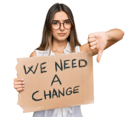 Young hispanic woman holding we need a change banner with angry face, negative sign showing dislike with thumbs down, rejection concept