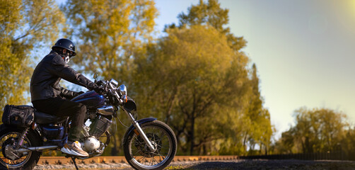 male motorcyclist in a leather jacket and helmet on a vintage custom motorcycle in nature. Concept...