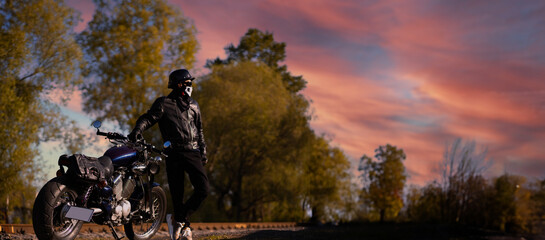 male motorcyclist in a leather jacket and helmet on a vintage custom motorcycle in nature. Concept of motorcycle life and the beginning of the season - obrazy, fototapety, plakaty