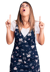 Young beautiful woman wearing casual floral dress amazed and surprised looking up and pointing with fingers and raised arms.