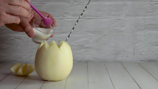 Melon with wine, white melvin, video, preparing, cocktail, adding, sugar. On white wooden table, stirrer. Originally from Chile, summer. Typical Chilean food and drink