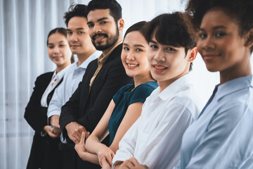 Fototapeta na wymiar Happy and smiling multiracial office worker hold hand in a line, promoting synergy and collaboration for business success. Diverse professional office worker bond at modern workplace. Concord