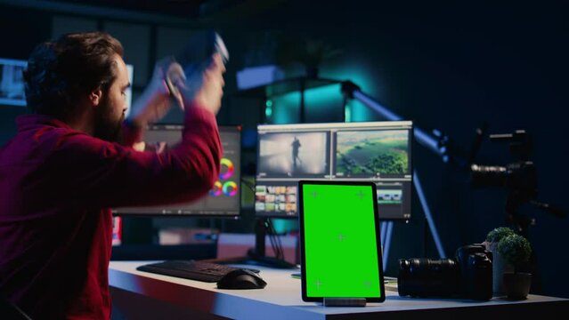 Green screen tablet on desk in studio next to video editor arranging recorded stock clips into seamless whole. Chroma key device near videographer assembling recorded footage into finished project