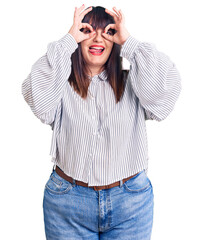 Fototapeta premium Young plus size woman wearing casual clothes doing ok gesture like binoculars sticking tongue out, eyes looking through fingers. crazy expression.